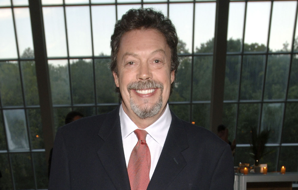 Tim Curry smiling at a public event, highlighting his enduring presence in entertainment