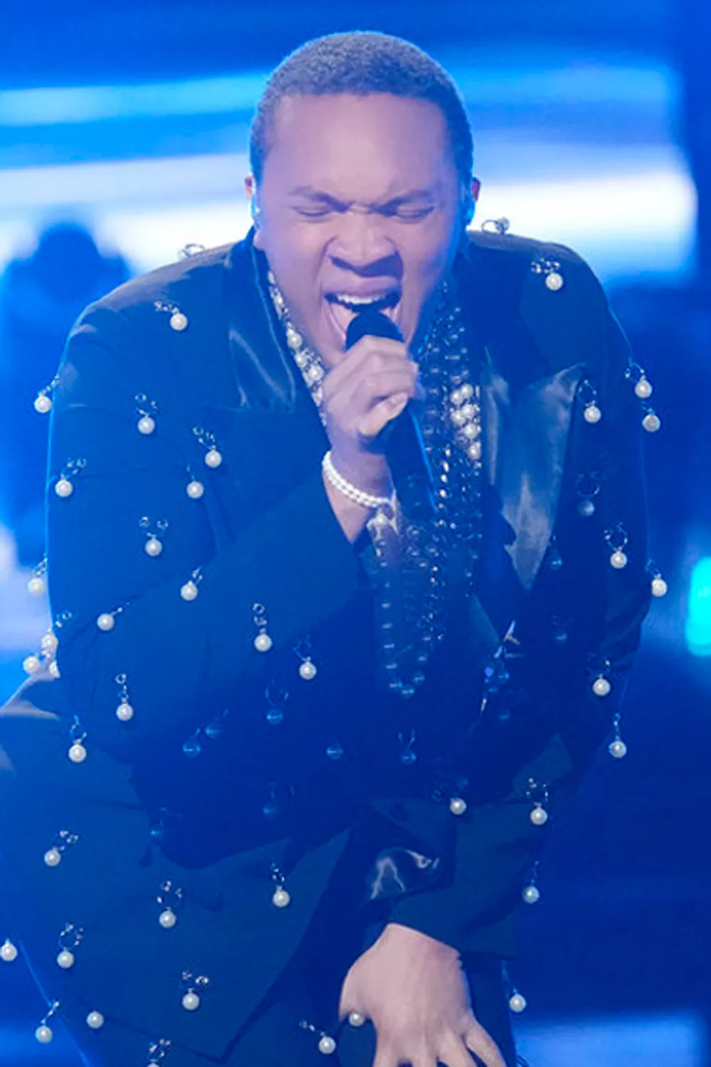 The finalists of The Voice Season 27 on stage, facing the judges and audience, with colorful lights illuminating the set